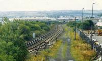 This view looks towards Fouldubs from the site of Grangemouth station. From left to right: lifted lines, lines to the oil terminal, former yards and docks, the site of Grangemouth No 3 box, out of use line (now lifted) to the docks (centre bottom) and the site of Grangemouth station. This was taken not long after removal of the box when signalposts still stood and the double track line had become two single track lines splitting at Fouldubs. The footbridge in the distance has been removed. (Compare with images 20698 and 7369).<br><br>[Ewan Crawford //1989]