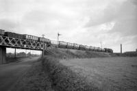 A coal train hauled by an ex-WD Austerity locomotive crosses the A907 Alloa - Dunfermline road on the old Helensfield bridge just east of Kincardine Junction in the 1960s on its way to Kincardine power station. The buildings to the right, standing on the edge of Clackmannan, are long demolished, as is Kincardine power station itself, although a new Helensfield bridge was hoisted into place in December 2006 as part of the Stirling - Alloa - Kincardine reopening project.<br><br>[Robin Barbour Collection (Courtesy Bruce McCartney) //]