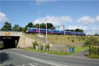 A First Trans-Pennine Express service for Manchester Airport leaves the WCML at Euxton Junction and heads to Manchester via Chorley and Bolton on 7 August 2009. The road in the foreground is the A49 former trunk road which passes under the WCML through a two part bridge. The older part (dating from the opening of the railway?) is known as Pack Saddle Bridge and is so narrow that traffic has to be controlled by traffic lights. It has also suffered from being struck on several occasions by road vehicles due to restrictions on height as well as width.<br><br>[John McIntyre 07/08/2009]