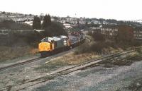 A Railfreight-liveried 37 hauls coiled steel up to Ebbw Vale for tin plating, circa 1988. It is approaching Park Junction - the line in the foreground used to go straight down to Newport docks, but since demolition of the bridge across the GW main line, was just a siding. I remember a leisurely Christmas lunch in the restaurant at the nearby Bassaleg station, when we ate in an old coach adjacent to the Machen line. Over two hours, a light engine came down from Machen, while one steel train went up to EV and another came down - good value! The hill on the left is called the Gaer - hence the tunnel and junction names.<br><br>[Ken Strachan //1988]