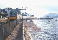 A late 1960s view of Fort William's then-classic lochside location. Opened by the West Highland Railway in 1894, the entire rail presence in this view was swept aside to accommodate the road builders, and the station was relocated in 1975 to an altogether more mundane location half a mile to the north east.<br><br>[Frank Spaven Collection (Courtesy David Spaven) //]