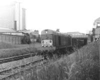 A southbound freight passes West Brompton LT station in June 1969 hauled by EE Type 1 locomotive no D8000. Photograph taken leaning over the fence alongside the northbound District Line platform 2, with the western edge of Earl's Court Arena visible on the right beyond the station roof. At that time the West London Line was still very much a cross-London freight corridor with no hint of the changes that would take place here 30 years later [see image 5126].<br><br>[John Furnevel 05/06/1969]