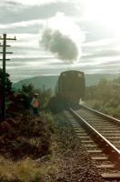 The track gang stands clear as the afternoon train from Aviemore to Boat of Garten comes out of the sun in the summer of 1980. [With thanks to John McIntyre] <br>
 <br><br>[Colin Miller //1980]