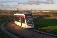 The low winter sun illuminates both the buildings of Edinburgh Airport in the background and the tram negotiating the sharp curve as it approaches the Ingliston Park and Ride stop en route to the city.<br><br>[Malcolm Chattwood 05/12/2014]
