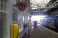 Scene at Stranraer on 26 August 2015, with the 1443 service to Kilmarnock at the platform and silk flowers by Louis Wall enlivening the station.<br><br>[John Yellowlees 26/08/2015]