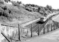Looking east towards the site of Stannergate station (closed 1916) between Dundee and Broughty Ferry in 1981, with an Aberdeen - Kings Cross HST approaching. The bridge linking the A92 (behind the trees on the left) and Stannergate Road has since been closed. The pylons visible have also gone, following the closure of Carolina Port power station on the other side of the bridge [see image 36084]. [Ref query 15197]<br><br>[John Furnevel 11/08/1981]
