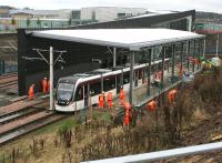 Work on the new tram platform at Edinburgh Gateway stops temporarily following the sound of the warning klaxon on 14 November as a wet tram emerges from under the A8 and passes by on its way to the airport. The new interchage is scheduled to open next month.<br><br>[John Furnevel 14/11/2016]