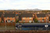 Early morning winter sunshine illuminates the houses of Jenks Loan in the foreground and the Pentland Hills in the background, as a southbound train on the Borders Railway pulls away from the platform at Newtongrange.<br><br>[John Furnevel 01/12/2016]