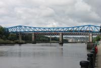 A 4-car Metro unit heads south over the Queen Elizabeth II bridge crossing the Tyne on 26th June 2017. The slight arc of the cantilevered Metro bridge allows a glimpse of a Virgin ECML train on the King Edward VII bridge behind. The bright blue paintwork of the bridge recreates the colour of the old Redheugh road bridge, replaced in the 1980s by a modern concrete structure, the pillars of which can be seen beyond the rail bridge. <br><br>[Mark Bartlett 26/06/2017]