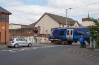 380111 crosses Princes Street on its way to Ardrossan Harbour. The crossing is protected with half barriers. On the left is a new building built on the site of the station building.<br><br>[Ewan Crawford 10/08/2017]