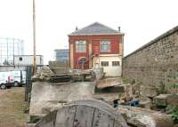 The former Granton Gasworks station in 2006, looking north along the staff platform. The arrival line ran straight through what was originally an open structure (the white wall with the 2 windows is a later addition) with staff able to access trains within the building. An internal stairway linked the platform to the station's upper level, from which a footbridge spanned the goods lines and yard leading to the extensive works area and offices that were once located off to the left.  The new Scottish Gas HQ stands in the background behind the former station, while the remains of the old gasometer, something of a landmark in this part of the world, can also be seen in the background.<br><br>[John Furnevel 16/8/2006]