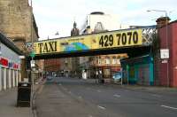 Looking west along the Gallowgate on a Sunday morning in April 2007 showing the viaduct carrying the CGU route between Saltmarket Junction (left) and High Street Junction. Just beyond the viaduct, Chrystal Bell's pub takes up the corner of Watson Street, while beyond that the Tollbooth Steeple stands at Glasgow Cross. Anyone leaving the pub after one too many should have no difficulty finding the number of the local taxi company.<br><br>[John Furnevel 01/04/2007]