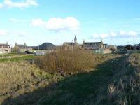 Site of Cairnbulg railway station, looking south-east towards St Combs. Part of the station site is now a bus-turning circle, but the trackbed can still be seen in the centre foreground, with the remains of the platform on the left . Remants of the goods loading bank can be seen at the far left. Behind the bus shelter is the former station masters house, now a private residence.<br><br>[John Williamson 24/02/2008]