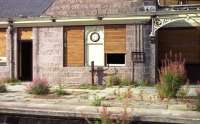 A close up of a part of the main station building at Banchory in August 1973, showing the remains of the station clock and platform weighbridge. Although the station had been boarded up at some time after closure in 1966, parts of the boarding had been removed in several places and damage had been caused to both the internal and external fabric of this once impressive station.<br>
<br><br>[John McIntyre /08/1973]