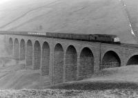 Shortly after emerging from the north portal of Blea Moor tunnel into Upper Dentdale the Settle and Carlisle line crosses two notable viaducts, the first at Dent Head and the second, seen here, at Arten Gill. The 657 feet long, 11 arch viaduct, completed in 1875, is built from  dark limestone obtained from the now disused quarries nearby. This stone, when polished, is known locally as <I>Dent marble</I>. The viaduct is pictured on a cold and overcast day in the winter of 1983/4 with traces of snow on the fells and a class 40 crossing southbound with a long parcels train.<br>
<br><br>[Colin Alexander //1994]