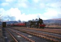 42737 with <I>Scottish Rambler No 3</I> at Beattock summit on 29 March 1964. On the left is the <I>private platform</I> and coach used by the <I>Siege</I> train which ran daily between the summit and Beattock station to enable families of railway workers living in cottages and hamlets along the way to do their shopping etc in Moffat. (The nickname derived from the <I>Siege of Mafeking</I> which was front page news in 1900 when the service started.) No date can been found for the official <I>closure</I> of the platform or withdrawal of the train, which was still running in 1965. One interesting bi-product of this service was that, in addition to the locomotive diagrammed to handle the train (invariably one of Beattock's bankers), any locomotive waiting to return to Beattock shed would be attached for the run back down the bank, so it was not uncommon for the southbound train to consist of 3 locomotives and 1 coach.<br><br>[Robin Barbour Collection (Courtesy Bruce McCartney) 29/03/1964]