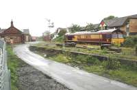 A light locomotive returns south through the closed Bedlington station on a wet afternoon in June 2004 after servicing Lynemouth Aluminium Works and North Blyth bauxite terminal. Bedlington South signal box and level crossing stand in the background, with Furnaceway Sidings beyond.<br><br>[Ewan Crawford 26/06/2004]