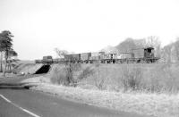 The thrice-weekly St Boswells - Greenlaw branch pickup goods west of Gordon at Easter time in 1965. The train is crossing the bridge over the A6105 (since removed) returning west towards Earlston. The two wagons being propelled by the diesel shunting locomotive are destined for Earlston sawmill. The outline of Greenknowe Tower, built by James Seton in 1581, can just be made out through the trees on the right. The Tower is now in the care of Historic Scotland.<br><br>[Bruce McCartney //1965]
