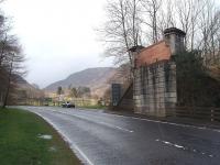 Immediately to the east of Lochearnhead station the line to St. Fillans crossed the road on a substantial bridge, of which only this east abutment remains although another bridge just beyond is still in place. The entrance to the scout camp, in the old station, is by the tree on the left in this view looking north along the Crianlarich road through Glen Ogle.<br><br>[Mark Bartlett 26/03/2009]