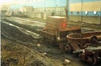 A wonderfully grim location. Round the back of the steelworks workshops and sandwiched between the building and the coal unloading sidings were some sidings at a lower level used to store redundant railway wagons and locomotives most of which were cut up as scrap steel. Near the camera is a (if I recall correctly) slag wagon formerly used in the ironworks during the tapping of a blast furnace and beyond by the JCB was a rail mounted crane and flatbed wagons. This crane did run, but turned the air black. The JCB was used to remove liquid coal from the tracks; coal mud tended to wash down over these sidings from the higher level sidings. It could get very close to the building. I often visited at lunchtime (my office was in the other side of the building) to see what interesting redundant equipment was around. Nothing of this scene remains today due to demolition and landscaping except a portion of the floor of the building and, intriguingly, a half buried slag wagon (this one?). The site has been overgrown since closure but redevelopment has started.<br><br>[Ewan Crawford //1988]