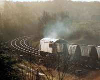 A low winter sun illuminates no 56030 near Crigglestone West station as it heads for Woolley Tunnel en route to Woolley Colliery with coal empties on a cold December morning in 1987, around the time the colliery was officially closed. Bordering on the districts of Barnsley and Wakefield, Woolley was one of the largest pits in West Yorkshire, employing approximately 2,000 men in 1980.  <br><br>[David Pesterfield 30/12/1987]