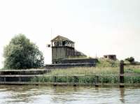 Rather like Stromeferry (no ferry) as the road sign says, here is Haddiscoe Swing Bridge (no bridge) signal box in Norfolk. Haddiscoe had 2 stations, the High Level station (renamed from Herringfleet Junction in 1904), shown here in July 1969, had been closed 10 years previously when services on the Yarmouth line were withdrawn. The Low Level station, on the line from Norwich to Lowestoft, is just off to the right. A complex junction existed here when both lines were operational and, following closure of the high level Yarmouth route, the former signal box at Haddiscoe Junction became an exhibit in the Science Museum, Kensington. The box is now housed at Mangapps Railway Museum, Burnham-on-Crouch.<br>
<br><br>[Colin Miller /07/1969]