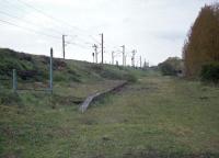 The Kelvedon and Tollesbury line in Essex was very lightly built and basic, such that there was little infrastructure left to survive after closure to passengers in 1951 and complete closure in 1962. This is the view of what remained at the Kelvedon Low Level terminus in March 1977. To the left was the steep descending connection from the GE main line, seen heading north east towards Colchester. The branch itself curved round to the right in the distance to cross the former A12. In the left foreground are the railings of the walkway to the upper station.<br><br>[Mark Dufton 30/04/1977]