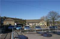 This is an attempt at a then and now shot of Holcombe Brook station [see image 21492]. The links with the past are the Peel Tower on the hill, the small hexagonal roof on the left of the shot and the top of the retaining wall seen just in front of the parked cars. Most of the wall is now hidden by the new building, the roof of which occupies the area where the track and buffers once stood. The station building was roughly where the 3 right hand cars are now parked.<br><br>[John McIntyre 29/03/2009]