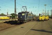 A DB Class 110 runs light engine through Hamm (Westfalen)in the sunshine early on a May morning in 1990. The yellow Deutsche Bundespost mail and parcel trollies brighten up the otherwise rather plain platforms.<br><br>[John McIntyre /05/1990]