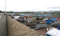 Photograph taken looking east from the pavement alongside the old Bathgate shed (just off picture to the right) on 28 August 2009. On the left is the A89 Edinburgh Road while over to the right a train has just left the current Bathgate terminus and is running alongside recently erected electrification masts on its way to Waverley. Between the road and the railway is part of the area currently being cleared in preparation for the construction of the new station, car parking, access roads and associated infrastructure. <br><br>[John Furnevel 28/08/2009]