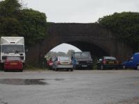 View in torrential rain of A539 road bridge over trackbed of former Wrexham to Ellesmere line, by former Overton on Dee Station, looking towards Wrexham. Large warehouse on station proper to right and timber yard to left possibly in old goods yard  <br><br>[David Pesterfield 06/10/2009]