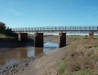 46 years after final closure of the Glasson Dock branch this fine bridge, over the tidal River Conder, still performs a useful role carrying a cycle track and footpath. Through the span Glasson Dock can be seen. It is still a busy small port with a regular freight service to the Isle of Man and a ship can just be seen moored at the outer quayside. <br><br>[Mark Bartlett 16/10/2009]