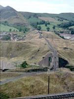 There's a lot of history in this picture.<br /><br>
<br /><br>
I took it in 1964 for the cable tramway carrying spoil up to the tip. In the foreground is the Taff Vale line to Merthyr; in the middle distance, beyond the buildings, is the embankment of the GWR/RR line from Quakers Yard to Merthyr.<br /><br>
<br /><br>
The building on the left is a school - destroyed in 1966 when the tip collapsed onto the village of Aberfan.<br><br>[John Thorn //1964]