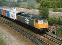 A class 47 on an Intermodal working runs alongside the partially lifted former Midland main line at Goose Hill Junction, Normanton, on 23 April 1988, heading west towards Wakefield. Alongside the loco stood Lockes Sidings signal box, with the brick rubble from a small building sited alongside [See image 38445]<br><br>[David Pesterfield 23/04/1988]