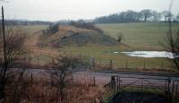 This view is from trackbed of the Wilsontown, Morningside and Coltness Railway immediately east of Morningside (NB) station, itself immediately east of an end on junction with the Caley and the Caley's Morningside station. The view shows the WMCR goods line curving off the 'main line' to serve the Coltness ironworks. The junction between the two was to the right. Traffic from pits to the east to the works was the raison d'etre of the line.<br /><br>
<br /><br>
At one time the much fought over WMCR was part of a Garnkirk and Glasgow Railway led route to Edinburgh (by through train from Glasgow Townhead to Longridge and by stagecoach from Longridge to Edinburgh) and the Caledonian Railway wanted it in preference to building its Shotts route, but it was not to be and no part of it remains open. But ... a short section (Polkemmet Junction to Bathgate Yard) of its later extension to Bathgate will be re-opened as part of the A-B route.<br><br>[Ewan Crawford /12/1987]