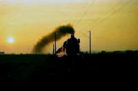 An eastbound heavy freight photographed in April 1976 passing Bruchmuhlen heading towards Bunde (Westfalen) in what was then West Germany, with the setting sun catching the smoke trail left by the locomotive.<br><br>[John McIntyre /04/1976]