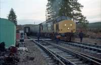 Early morning at Tulloch during Christmas 1987. The northbound sleeper, hauled by 37423, has drawn forward of the crossing between platforms due to its length. At the southbound platform is the morning train for Glasgow (37407 <i>Loch Long</i>). The train crews swap over across the tracks (they also guided a dismounting passenger). Slippery diesel was spilled all over the footway so crunching across the ballast might have been a better option anyway. Tulloch was very much in use as a maintenance base at the time, with lots of equipment lying alongside the platers hut on the left.<br><br>[Ewan Crawford 29/12/1987]