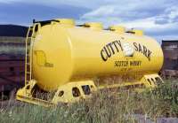 A striking example of advertising on rail. A demountable tank container for the local grain distillery sidings sits in Invergordon goods yard in 1974.<br>
<br><br>[David Spaven //1974]