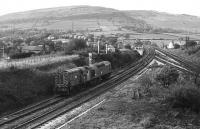 On a journey that would now be made by road lowloader, a Class 25 hauls an 08 shunter (minus coupling rods) through Chinley North Junction. The train is coming off the Peak Forest line, and is signalled to join the slow line of the four track section. Presumably the 08 is going for workshop or depot attention. The Midland Railway signalbox seen here was replaced by a BR pattern box soon after this picture was taken and the junction at Chinley North has since been considerably simplified. <br><br>[Mark Bartlett //1979]