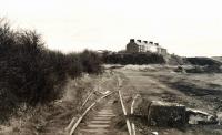 The since-lifted remains of Lammerlaws Yard, to the east of Burntisland docks, looking east on 31 March 2002 with the rocky promontory of Lammerlaws itself in the background. At this stage these tracks were still physically connected to the mainline as were all remaining tracks in the docks area. Then a mobile phone station was built on the access from the main line. The junction itself was finally severed in 2009 after many years of disuse, though a signal controlling access to the main line remained in place and lit until 2008.<br><br>[David Panton 31/03/2002]