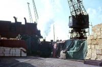 One of the Preston Dock fleet of Bagnall 0-6-0ST locos picks its way between the quayside cargoes and cranes. A small freighter can just be seen behind the locomotive. The dock itself is now a marina, and retail and residential developments have sprung up on the areas formerly used for cargo handling.<br><br>[David Hindle //1968]