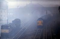 Two Class 37 locomotives, 37055 and 37140, appear out of the mist with a tanker train heading east out of Healey Mills yard in 1979. The train is passing the old Horbury and Ossett station where 08098 is travelling back to Healey Mills with 9K47, a trip working bringing repaired trucks from Wakefield wagon repair shops back to the yard [see image 23602]. This long lens view was from Addingford Lane bridge in Horbury cutting. [Thanks to Wyn Garnett, former Healey Mills shunter, for local information.]  <br><br>[Mark Bartlett 10/04/1979]