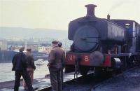 Something has caught the eye of the workers at Whitehaven Harbour as Barclay 0-4-0ST No. 8 simmers on the quayside. Whitehaven exported coal from nearby collieries, including Saltom, Lady pit, King, Duke, Wellington, Haig and Kells and a 21T hopper wagon is coupled to the locomotive. Nowadays the harbour is a marina and has a lock gate so that it doesn't empty at low tide. All quayside railway lines have been removed. (With thanks to Chris Gomersall for local information).  <br><br>[David Hindle //1968]