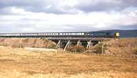 A Class 40 takes a southbound train over the wooden trestle bridge at Aultnaslanach, just north of Moy, in 1976. Class 40s became regular traction on the Highland Main Line in the mid-1970s, but were never a great success. Their weight and gearing did not suit this heavily-graded route - the photographer's son recollects one particular occasion on a southbound train when a Type 4's speed on the climb to Slochd Summit dropped to less than 15mph. The notable wooden bridge in the photograph was first crossed by a train in 1897 and is the last of its type to carry a main line in Scotland. A major project aimed at ensuring the long-term viability of this historic structure was undertaken in 2003 [see image 20481].<br>
<br><br>[Frank Spaven Collection (Courtesy David Spaven) //1976]