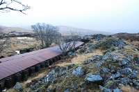 View south over the southern half of the Cruach Rock Snowshed. This is a covered cutting running north 205 yards from a girder overbridge. The roof is made of corrugated iron laid over a structure built of old rails with two walls built on either side of the cutting. There is a central portion which can be lifted off in the summer and replaced to keep the snow out of the cutting. When a train passes some of the central portions are lifted by the dam of air pushed by the train. Spoil from the cutting can be seen on the right.<br><br>[Ewan Crawford 15/02/2010]