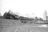 St Margarets V2 2-6-2 no 60816 with a northbound freight on the Waverley route in the 1960s. The locomotive has just crossed the bridge over the Kershope Burn, with the border signs located on the embankment on either side. Kershopefoot signal box stands in the background and half of the freight is yet to clear the level crossing at the north end of the station. [See image 26820]<br>
<br><br>[K A Gray //]