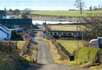 Looking south along the unclassified road at Ardmore Point towards the River Clyde on 1 March 2010. The barriers are down at Ardmore East level crossing as a Glasgow bound Class 320 passes.<br><br>[John McIntyre 01/03/2010]