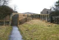 Pedestrian access to the site of Bowes station on 20 March 2010. The steps up from alongside the A67 cross a farm access road half way, on the far side of which a second flight leads up to the station itself. Part of the remains can be seen just above the steps [see image 28262], while the medieval castle - like structure on the right is in fact the remains of a goods shed. Between the two ruins is the roof of a large farm building that now stands on the trackbed.<br><br>[John Furnevel 20/03/2010]