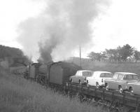 A double-headed train of Ford cars, featuring Corsair and Anglia models, on the southern approach to Newcastleton on the Waverley route around 1964. The train is the 10.15 (SO) Ditton Junction - Bathgate and the locomotives 61404+61134.<br><br>[K A Gray //1964]