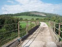 A tramroad was built to carry limestone from the quarry at Warton to the Ironworks at Carnforth and a spur was used for tipping slag alongside the River Keer estuary. A long section of the old formation is now used as a farm road and is seen here in July 2010 crossing the Cumbrian Coast railway and then curving round with Warton Crag Quarry visible behind [See image 30144] for the view in the opposite direction. [Photographed with landowner's permission.]<br><br>[Mark Bartlett 23/07/2010]